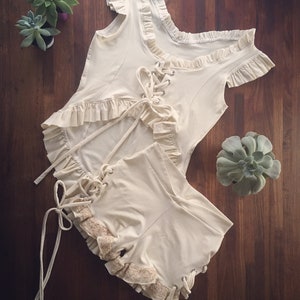 May include: A white lace-up top and shorts set with ruffled trim. The top has a scoop neck and short sleeves. The shorts have a high waist and are fitted.