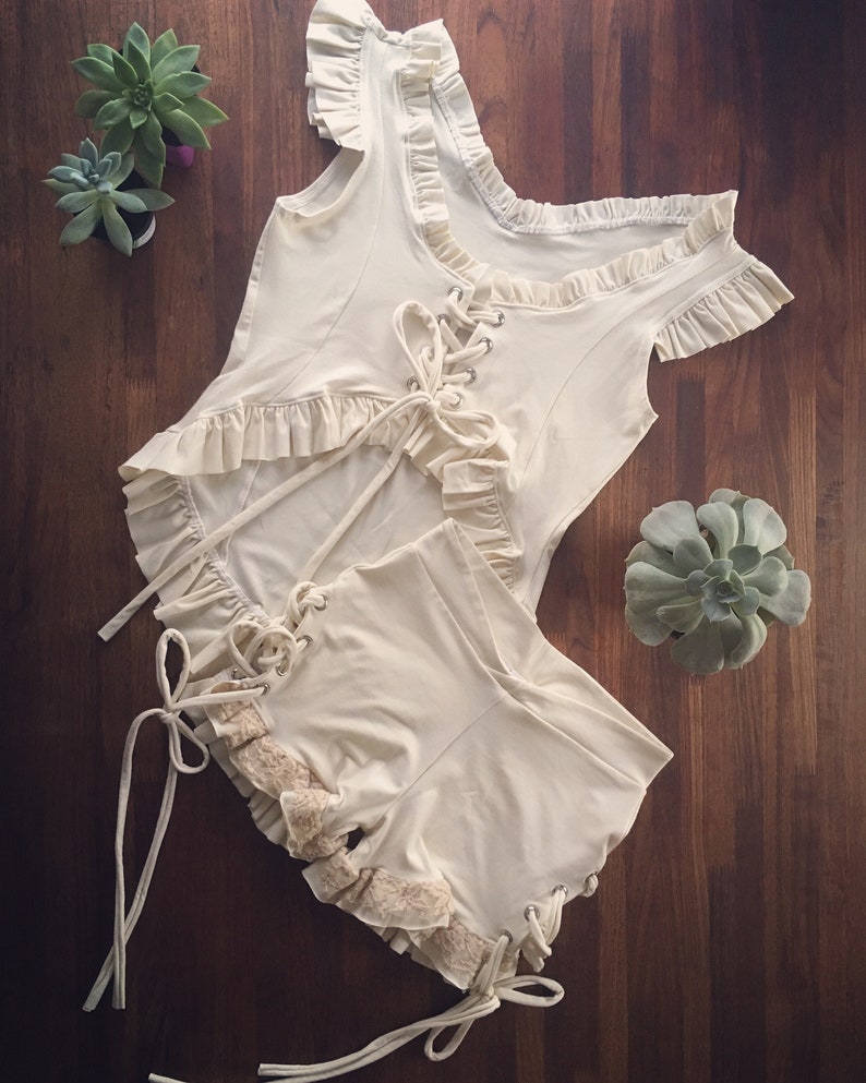 May include: A white lace-up top and shorts set with ruffled trim. The top has a scoop neck and short sleeves. The shorts have a high waist and are fitted.
