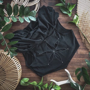 May include: A black hooded top with a large flower design on the back. The flower is made of white stitching and has a silver button in the center.