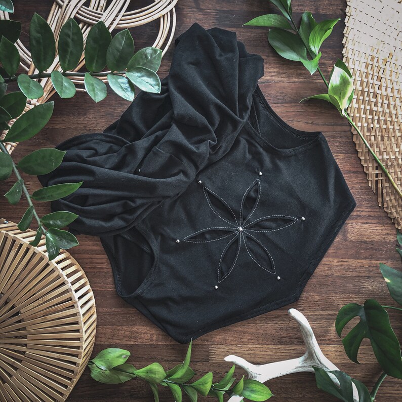 May include: A black hooded top with a large flower design on the back. The flower is made of white stitching and has a silver button in the center.