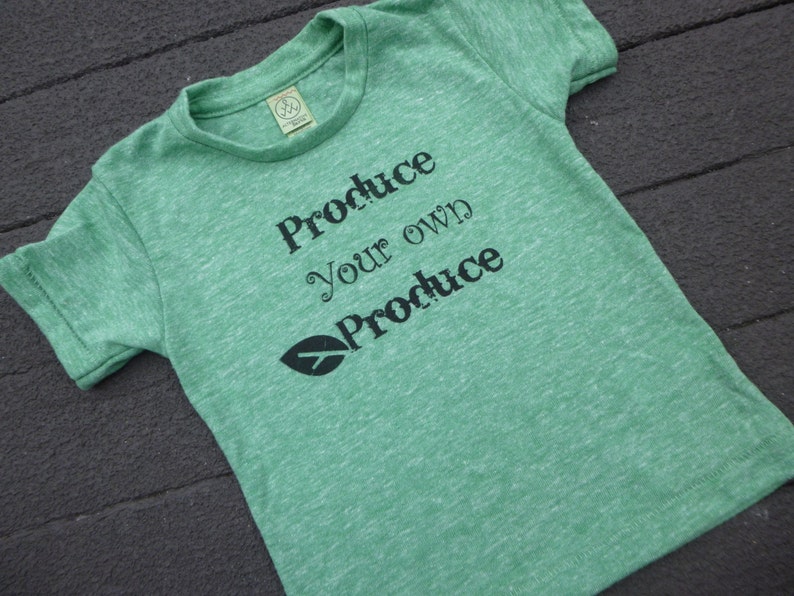 Op de afbeelding: Groen T-shirt met de tekst "Produce your own Produce" en een kleine bladgrafiek.