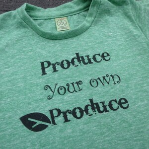 Op de afbeelding: Groen T-shirt met een zwart bladerenlogo en de tekst "Produce your own Produce" gedrukt op de voorkant.