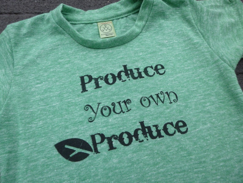 Op de afbeelding: Groen T-shirt met een zwart bladerenlogo en de tekst "Produce your own Produce" gedrukt op de voorkant.