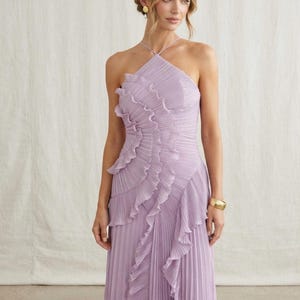 May include: A floor-length lavender dress featuring a halter neckline with thin straps, a fully pleated fabric construction, and a prominent vertical ruffle detail that cascades diagonally from the bodice down to the hem of the skirt.