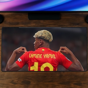 Peut inclure: Un tapis de bureau rectangulaire présentant une impression graphique d'un joueur de football vu de dos, portant un maillot rouge avec le nom LAMINE YAMAL et le numéro 10 imprimés en jaune. Le joueur a des cheveux courts clairs et tient le maillot.