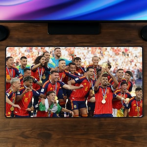 May include: A rectangular desk mat featuring a high-resolution photograph of the Spanish national soccer team celebrating a victory. The players are wearing red jerseys and gold medals, with one player holding a gold trophy aloft in the center.