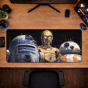 Peut inclure: Tapis de souris rectangulaire noir avec un design Star Wars représentant R2-D2, C-3PO et BB-8. L'illustration est stylisée sur fond noir. Le tapis est sur un bureau en bois avec des accessoires informatiques.
