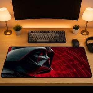 Könnte beinhalten: Rechteckiges Mauspad mit einer detaillierten Grafik von Darth Vaders Helm in Schwarz und Grau, vor einem roten Hintergrund mit radialem Design. Das Pad liegt auf einem Holzschreibtisch mit Tastatur, Maus und Kopfhörern.