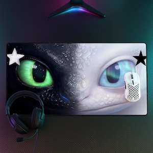 Puede incluir: Una alfombrilla de escritorio rectangular con un diseño de cara dividida de un dragón negro con un ojo verde brillante y un dragón blanco con un ojo azul claro. Una estrella blanca a la izquierda, una estrella negra a la derecha, un ratón blanco y auriculares negros.
