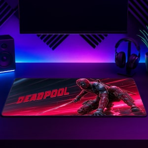 Può includere: Un tappetino per mouse rettangolare da gaming con un'illustrazione dinamica del personaggio Deadpool in una posa di combattimento accovacciata. Il design include la scritta DEADPOOL in lettere rosse su uno sfondo scuro con strisce luminose.