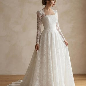 May include: A floor-length white lace gown featuring long sleeves, a square neckline, and a fitted bodice that transitions into a full, flowing skirt with a train. The intricate floral lace pattern covers the entire garment from the shoulders down.
