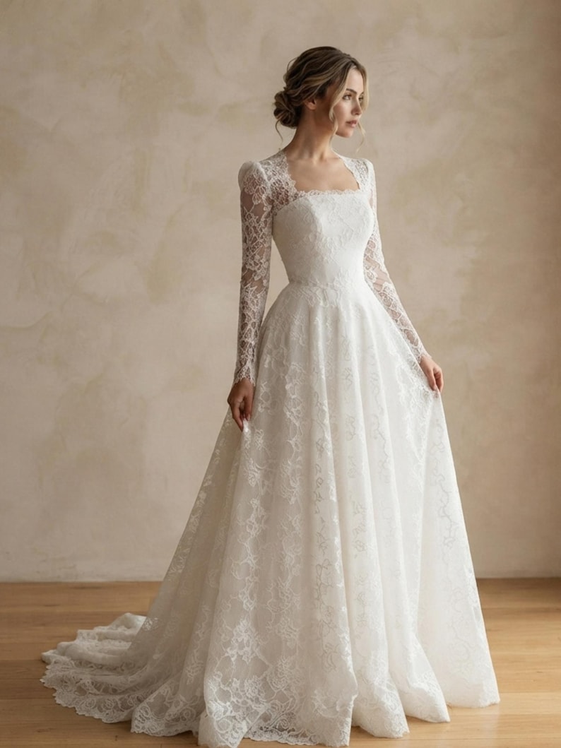 May include: A floor-length white lace gown featuring long sleeves, a square neckline, and a fitted bodice that transitions into a full, flowing skirt with a train. The intricate floral lace pattern covers the entire garment from the shoulders down.