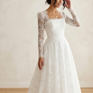 May include: A floor-length white gown featuring long, sheer lace sleeves and a square neckline. The bodice and skirt are adorned with a delicate floral lace overlay, creating a textured pattern throughout the garment from the shoulders to the hem.
