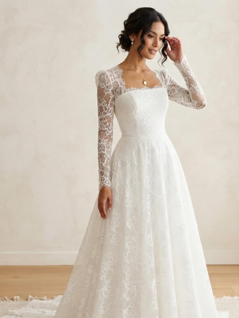 May include: A floor-length white gown featuring long, sheer lace sleeves and a square neckline. The bodice and skirt are adorned with a delicate floral lace overlay, creating a textured pattern throughout the garment from the shoulders to the hem.