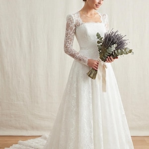 May include: A floor-length white wedding dress featuring long lace sleeves, a square neckline, and a fitted bodice that transitions into a full skirt with a train. The dress is adorned with intricate floral lace patterns throughout the fabric.