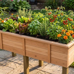 May include: A rectangular raised garden bed constructed from light brown horizontal wooden planks with four sturdy vertical legs, filled with dark soil and planted with various green leafy vegetables, herbs, and bright orange marigold flowers.