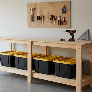 May include: A light-colored wooden workbench with a lower shelf holding four black storage bins with yellow lids. A pegboard above displays various hand tools, while a cordless drill, tape measure, and triangle square sit on the surface.