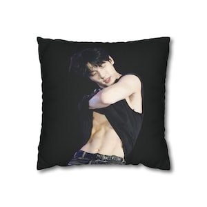 May include: A square throw pillow featuring a photographic print of a person with dark hair wearing a black sleeveless shirt that is lifted to reveal their midriff. The person is positioned against a solid black background on the pillow cover.