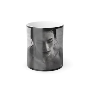 May include: A cylindrical ceramic mug featuring a black and white photographic print of a person with wet hair and skin. The mug has a white interior and a black rim, showcasing a high-contrast portrait that wraps around the exterior surface.
