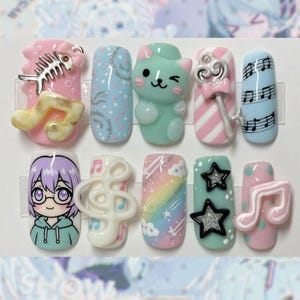 May include: A set of ten press-on nails featuring colorful designs including a fish skeleton, a mint green cat, a silver key, musical notes, a cartoon character with purple hair, a rainbow with clouds, and black glitter stars on pastel backgrounds.