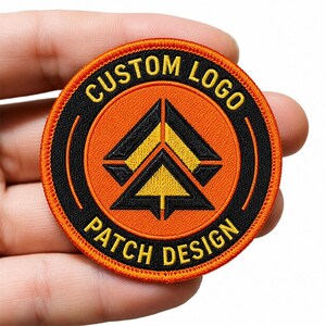May include: A circular embroidered patch featuring a bright orange center with a black and yellow geometric arrow design. The black border contains the yellow text CUSTOM LOGO at the top and PATCH DESIGN at the bottom, finished with an orange edge.