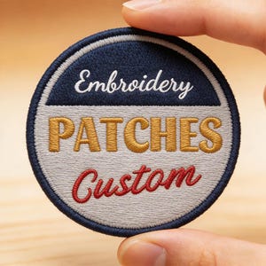 Peut inclure: Un écusson brodé circulaire présentant une section supérieure bleu foncé avec le texte blanc Embroidery, un centre gris clair avec le texte doré PATCHES, et une section inférieure avec le texte rouge en cursive Custom, bordé de bleu foncé.