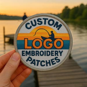 Könnte beinhalten: Ein runder gestickter Aufnäher mit einer Sonnenuntergangslandschaft und einer angelnden Person in einem Boot. Der Text lautet CUSTOM LOGO EMBROIDERY PATCHES in dunkelblauer Schrift. Das Design enthält horizontale Streifen in Gelb, Orange und Blaugrün.