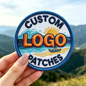 May include: A circular embroidered patch with a blue border featuring the text CUSTOM LOGO PATCHES in dark blue. The design includes a yellow sun, orange lettering, a blue sailboat on a light blue sea, and a tan beach against a white background.