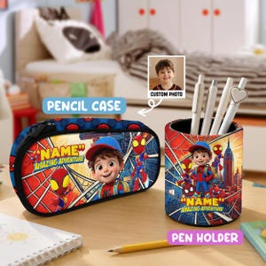 May include: A cylindrical pen holder and an oval pencil case featuring a cartoon character in a red and blue superhero suit, a cityscape background, and the text "NAME" and "AMAZING ADVENTURE". The items include a custom photo insert.