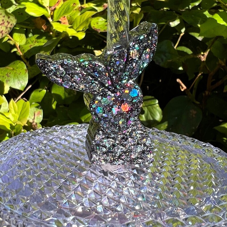 May include: A black glitter mermaid tail bottle stopper with iridescent glitter accents. The tail is sitting on a clear, textured surface.
