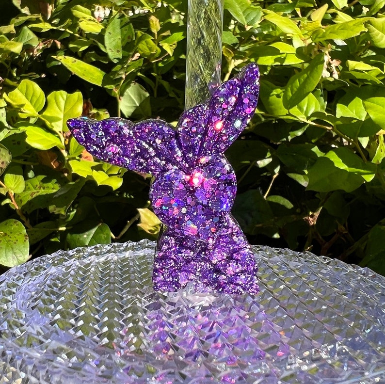 May include: Purple glitter resin bunny rabbit figurine. The bunny is standing on a clear glass surface.