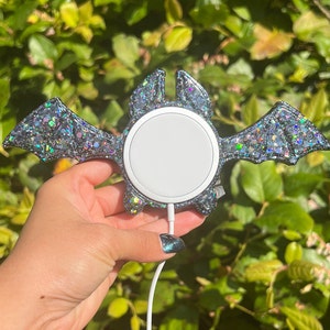 May include: A black and silver glitter bat-shaped phone charger stand with a white wireless charging pad.