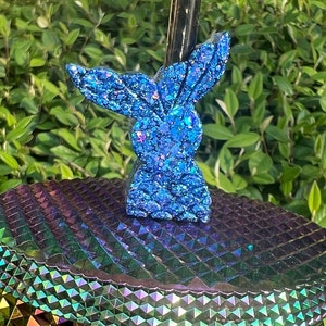 May include: A blue glitter bunny rabbit figurine with a sparkly finish. The figurine is sitting on a iridescent surface.