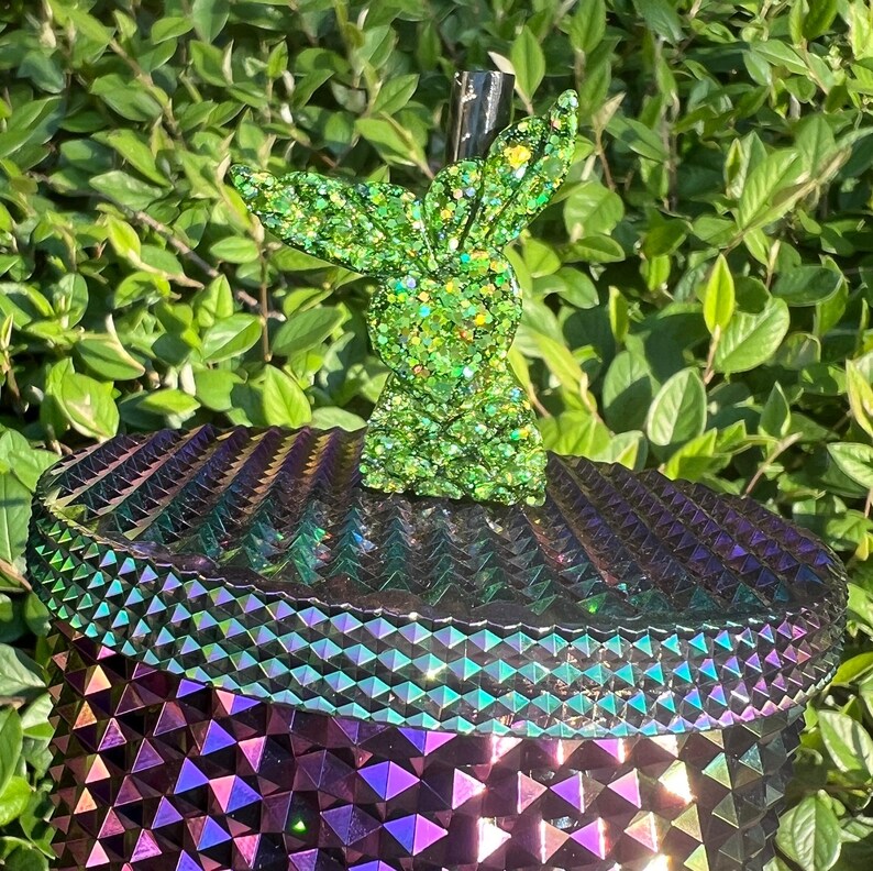 May include: A green glitter resin bunny rabbit figurine with a iridescent purple and green geometric patterned base.