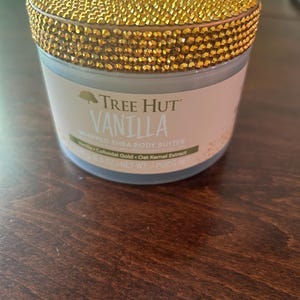 May include: A jar of Tree Hut Vanilla Whipped Shea Body Butter. The jar has a gold, jewel-encrusted lid. The label reads "Vanilla" and lists ingredients. The net weight is 8.4 oz.