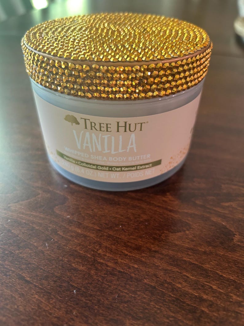 May include: A jar of Tree Hut Vanilla Whipped Shea Body Butter. The jar has a gold, jewel-encrusted lid. The label reads "Vanilla" and lists ingredients. The net weight is 8.4 oz.