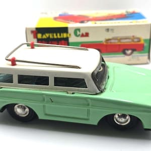 Könnte beinhalten: Ein Vintage-Blechspielzeug-Kombi mit hellgrüner Karosserie, weißem Dach und silbernem Metalldachträger. Das Spielzeugauto hat schwarze Räder mit silbernen Radkappen und wird mit der originalen Pappschachtel mit der Aufschrift Travelling Car geliefert.