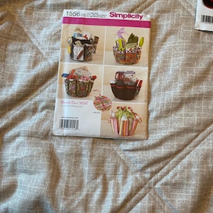 May include: A Simplicity sewing pattern envelope 1556 featuring illustrations of various fabric buckets with multiple exterior pockets. The cover displays several designs including floral, striped, and solid black patterns, with the text Buckets Gone Wild.