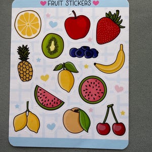 Può includere: Un foglio di adesivi rettangolare con il testo FRUIT STICKERS che presenta illustrazioni di una fetta di limone, mela, fragola, ananas, kiwi, mirtilli, banana, fetta di anguria, anguria intera, due limoni, pesca e ciliegie su uno sfondo a griglia.
