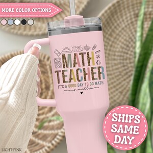 May include: A light pink stainless steel tumbler with a handle and clear lid. The front features the text "MATH TEACHER" in a leopard print pattern, "IT'S A GOOD DAY TO DO MATH" in black, and "ms. miller" with a small heart icon below.