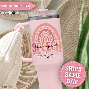 May include: A light pink insulated tumbler with a handle and a clear lid. The front features a graphic of a rainbow with hearts and the text "SPEECH therapist EVERYONE DESERVES A VOICE" followed by the name "jessica" and a small heart icon.