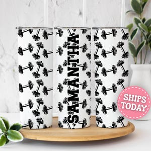 May include: A white cylindrical tumbler featuring a repeating black dumbbell pattern and the name SAMANTHA printed vertically in bold black capital letters. The drinkware includes a clear lid and a straw, showcasing a clean, high-contrast design.