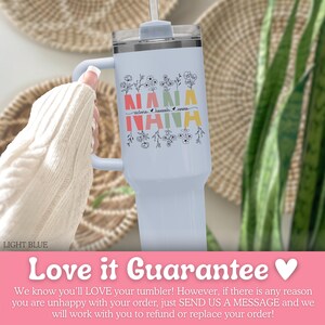 May include: A light blue tumbler with a handle and a clear lid featuring the word NANA in red, yellow, and green block letters. The design includes black line art of wildflowers above and below the text, with the names Victoria, Hannah, and Emma.