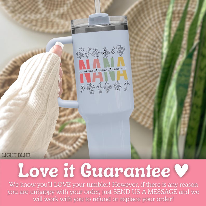 May include: A light blue tumbler with a handle and a clear lid featuring the word NANA in red, yellow, and green block letters. The design includes black line art of wildflowers above and below the text, with the names Victoria, Hannah, and Emma.