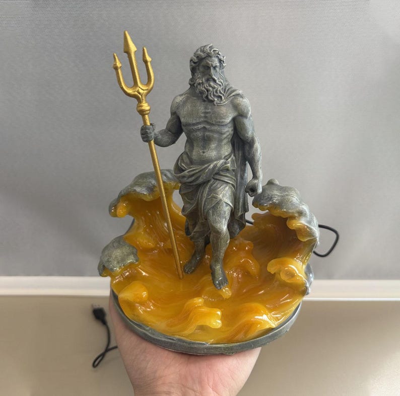 K&ouml;nnte beinhalten: Eine Statue des griechischen Gottes Poseidon, der einen goldenen Dreizack h&auml;lt. Die Statue ist grau und steht auf einer Basis aus gelben Wellen. Die Basis hat einen dunkelgrauen Rand. Ein Netzkabel ist sichtbar.