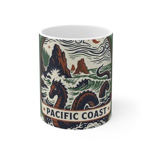 May include: White ceramic mug with a design depicting a sea serpent in the ocean, with the text "PACIFIC COAST". The illustration uses brown, green, and cream tones, with waves, mountains, and a crescent moon.