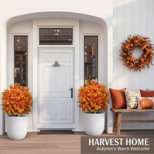 May include: A white front door with a black knocker, flanked by two white planters containing orange autumn foliage. A wreath of orange leaves and pumpkins hangs on the wall above a wooden bench with orange and patterned pillows. Text reads HARVEST HOME.