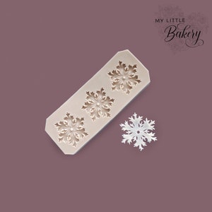 Può includere: Uno stampo in silicone con tre disegni di fiocchi di neve. Lo stampo è marrone chiaro e i fiocchi di neve sono bianchi. Lo stampo è su uno sfondo viola. Il testo "My Little Bakery" è nell'angolo in alto a destra dell'immagine.