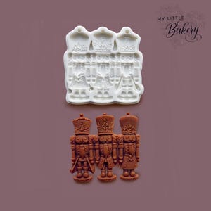 May include: A white silicone mold and three brown nutcracker figures. The mold features three nutcracker soldiers with detailed uniforms. The brown figures are made from the mold, showcasing intricate details of the nutcracker design.