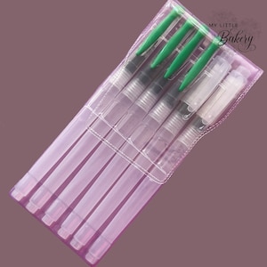 Könnte beinhalten: Ein Set mit sechs transparenten Aquarellpinseln mit grünen Kappen, verpackt in einer transparenten Plastikhülle. Die Verpackung trägt den Text "My Little Bakery".